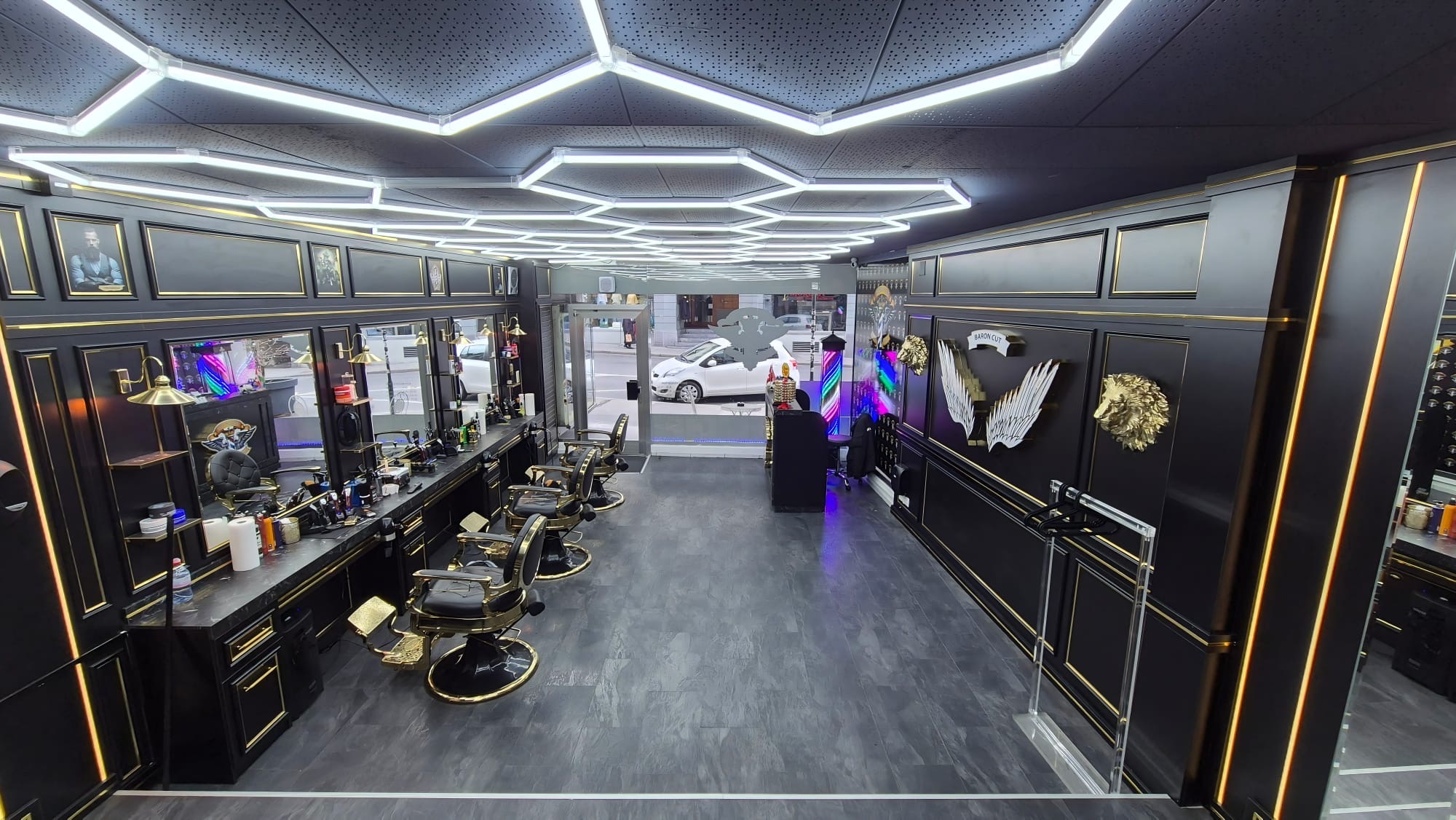 Salon von Baron Cut: schwarze Wände mit goldenen Leisten, Barberstühle in Schwarz und Gold, Wabenlicht an der Decke